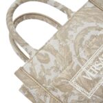 The Versace Barocco Athena Extra Small Tote Bag is an exquisite fusion of opulence, sophistication, and timeless elegance. Crafted with meticulous attention to detail, this iconic piece encapsulates the essence of the Versace brand, showcasing its signature Barocco motif and distinctive design elements. At first glance, the bag exudes a sense of luxury, boasting a striking combination of rich textures and vibrant hues. The Barocco motif, synonymous with Versace's heritage, adorns the exterior of the bag, intricately woven into the fabric with precision and finesse. Its bold and intricate patterns pay homage to classical Greek and Roman art, adding a touch of regal grandeur to the design. Constructed from premium materials of the highest quality, the tote bag is both durable and luxurious. The supple leather exterior is soft to the touch, while the gleaming gold-tone hardware adds a touch of glamour and refinement. The structured silhouette maintains its shape effortlessly, exuding an air of sophistication and poise. Practical yet stylish, the Extra Small Tote Bag is designed to cater to the modern woman's lifestyle. Despite its compact size, the interior offers ample space to accommodate essentials such as keys, phone, wallet, and makeup, making it ideal for both day-to-day use and special occasions. The interior is lined with sumptuous satin fabric, providing a luxurious backdrop for your belongings. Versatility is another hallmark of this timeless accessory. Whether carried by the top handles for a polished look or slung over the shoulder using the detachable strap for added convenience, the tote bag effortlessly transitions from day to night, complementing any ensemble with effortless sophistication. In conclusion, the Versace Barocco Athena Extra Small Tote Bag is a true masterpiece that embodies the epitome of luxury and style. With its exquisite craftsmanship, iconic design, and practical functionality, it is more than just a fashion accessory—it is a symbol of prestige, refinement, and enduring elegance.